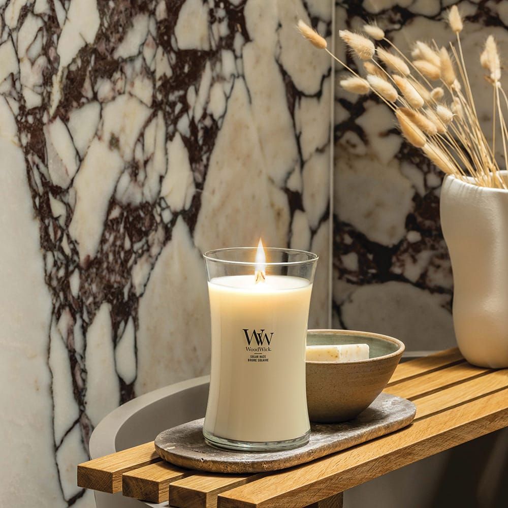 Candela accesa. Logo WoodWick. Su vassoio di legno, accanto a ciotola. Sfondo: marmo.