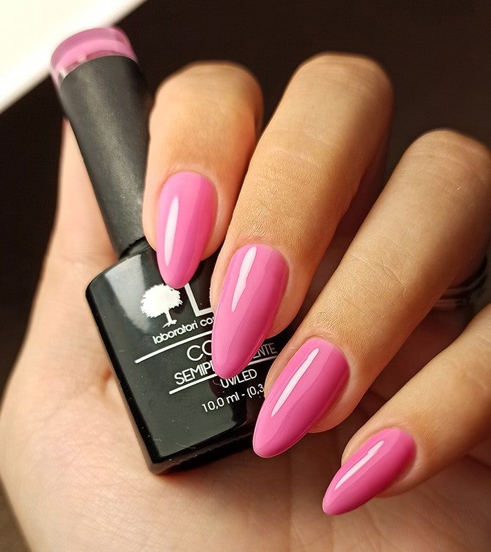 Mano con unghie rosa smaltate. Flacone di smalto con tappo nero. Unghie a mandorla.