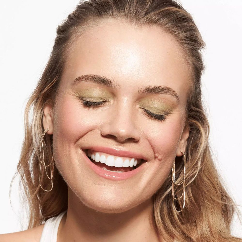 Primo piano di una donna sorridente con trucco e orecchini d'oro.