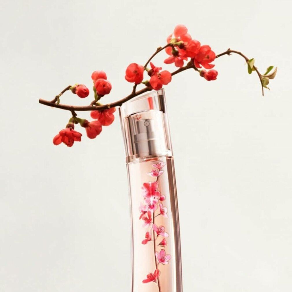 Flacone di profumo con design floreale, con ramo fiorito. Flacone con contenuto rosa e motivo floreale. Forma inclinata.