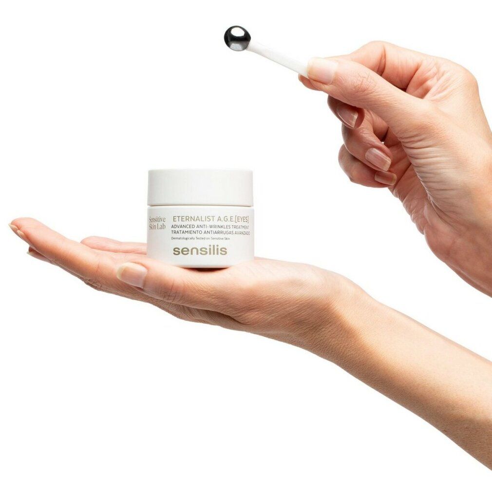 Mano che tiene vasetto bianco Sensilis e applicatore. Testo: Eternalist A.G.E.[EYES]. Testato dermatologicamente.