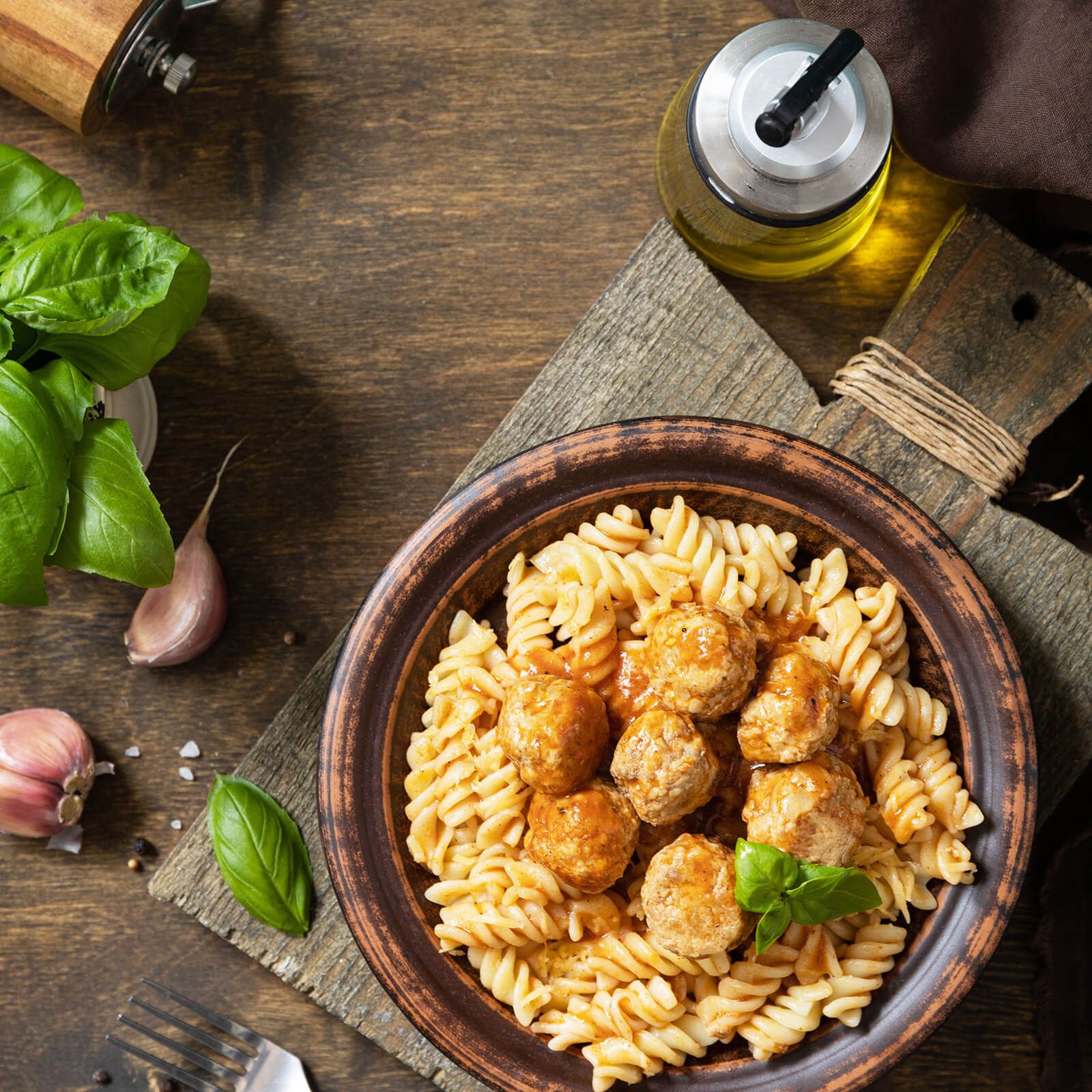 Piatto di fusilli con polpette in una ciotola marrone. Su tavolo di legno, con ingredienti.