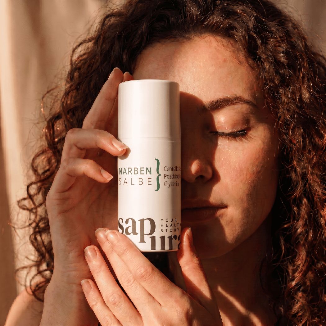 Una donna tiene un flacone bianco con pompa 'Narbensalbe' davanti al viso.