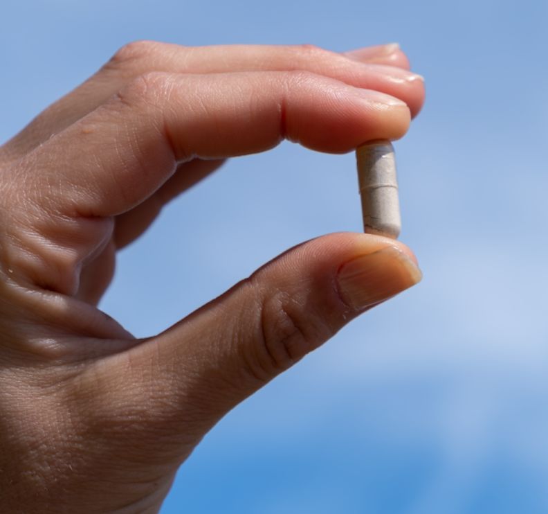 Dita che tengono una singola capsula Aavalabs Ashwagandha davanti al cielo blu.