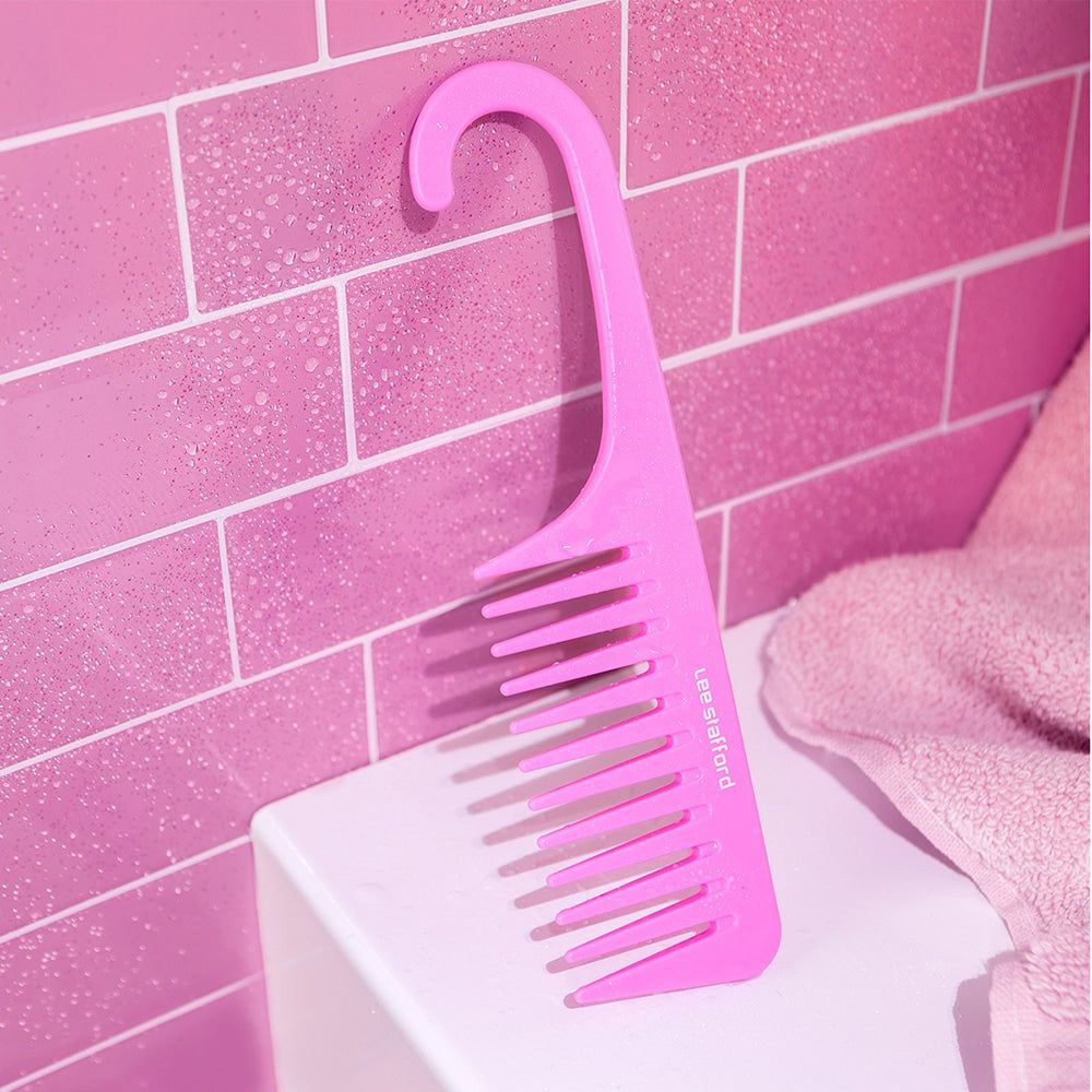 Un pettine rosa a denti larghi appeso a una parete piastrellata.