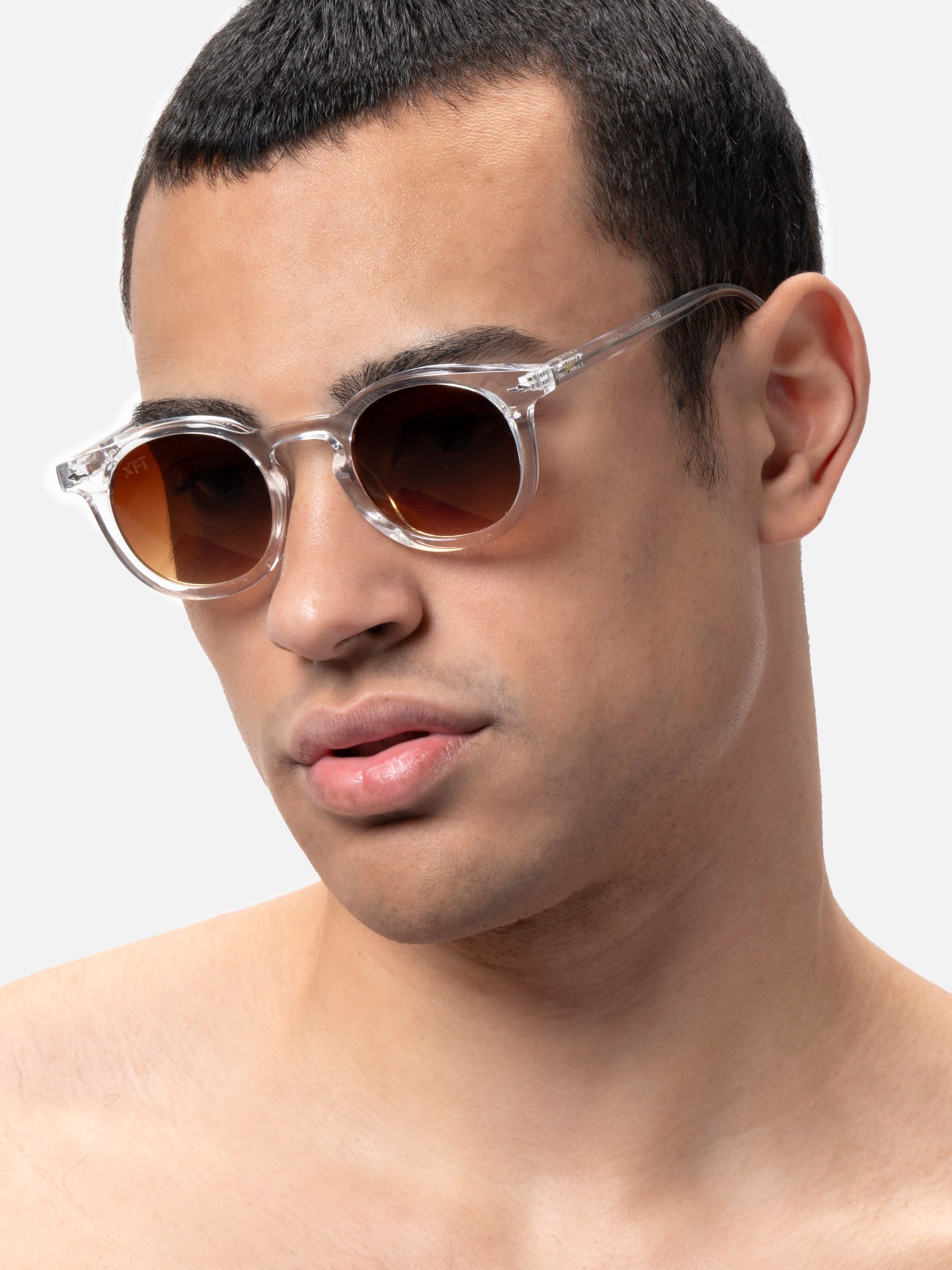 Uomo con occhiali da sole con montatura trasparente e lenti marroni. Primo piano, vista laterale.