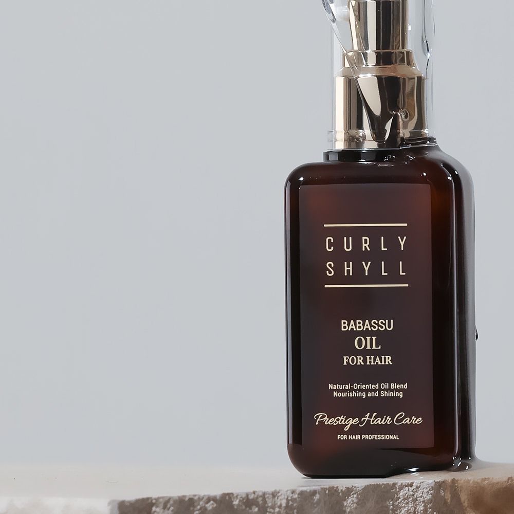 Flacone in vetro marrone con vaporizzatore dorato. Scritta: CURLY SHYLL, BABASSU OIL FOR HAIR, Prestige Hair Care.