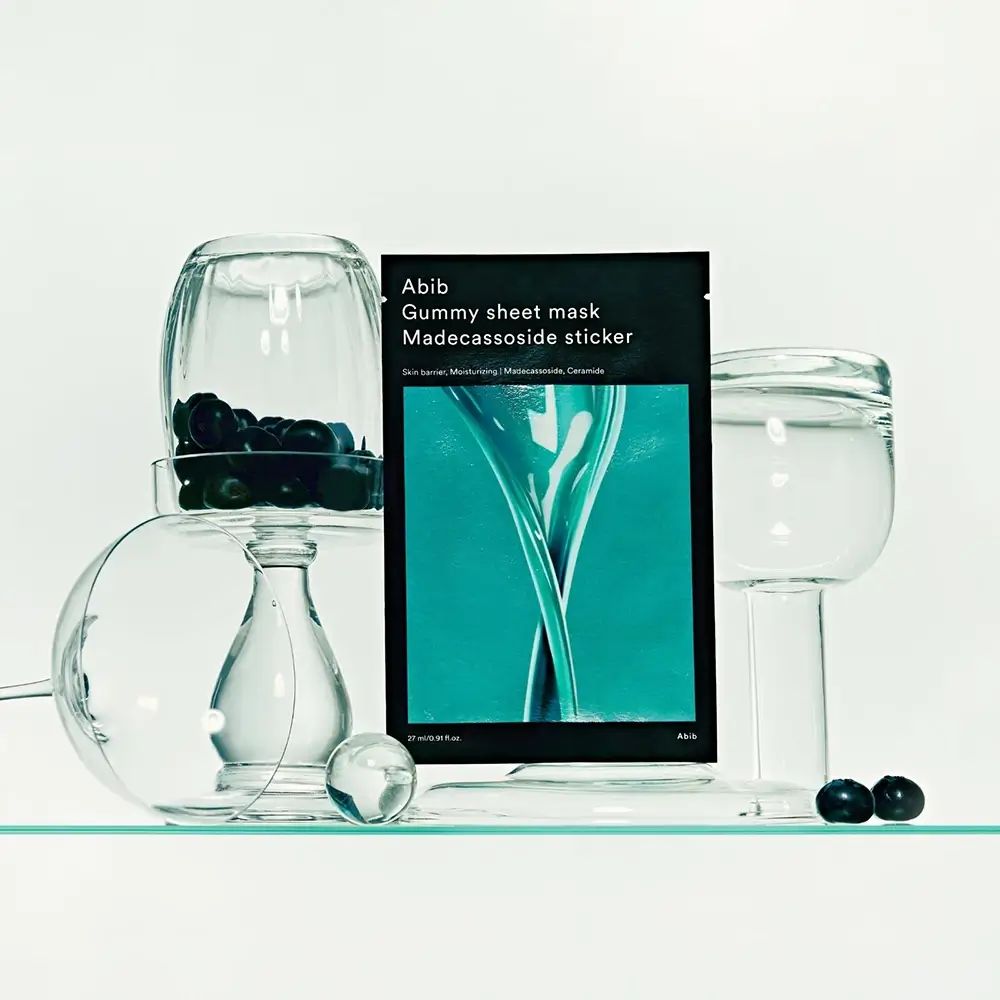Abib Gummy Sheet Mask Madecassoside Sticker tra contenitori di vetro con mirtilli.