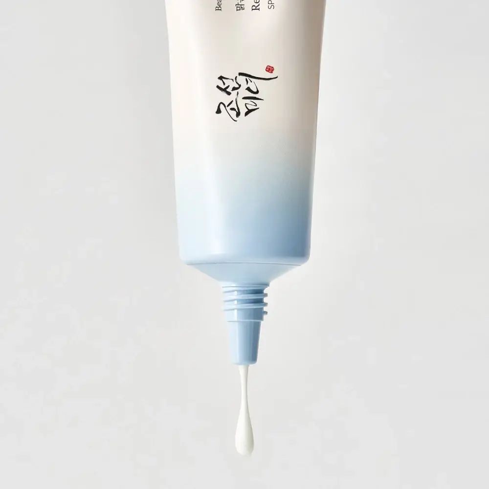 Tubo da cui gocciola crema. Tappo blu. Sfondo bianco.