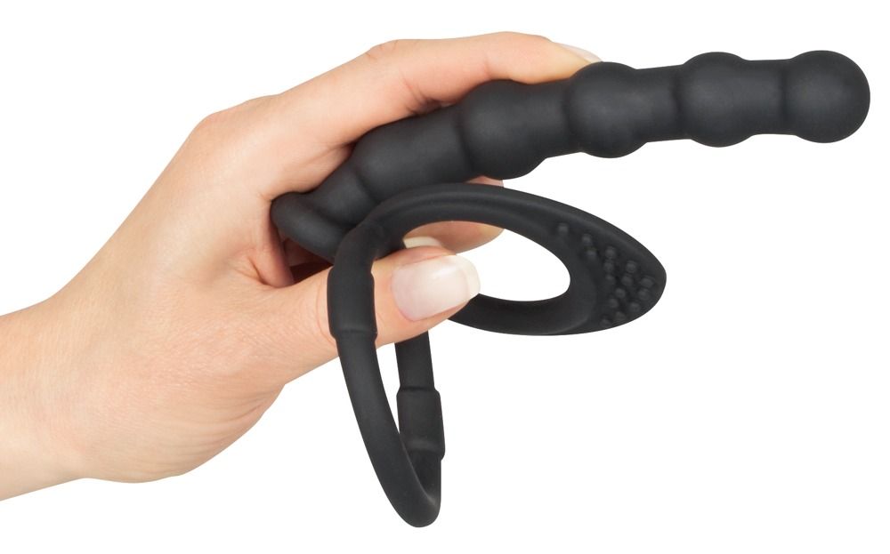 Mano che tiene anello per pene/testicoli nero con dildo anale. Anello con rilievi, dildo scanalato. Silicone.