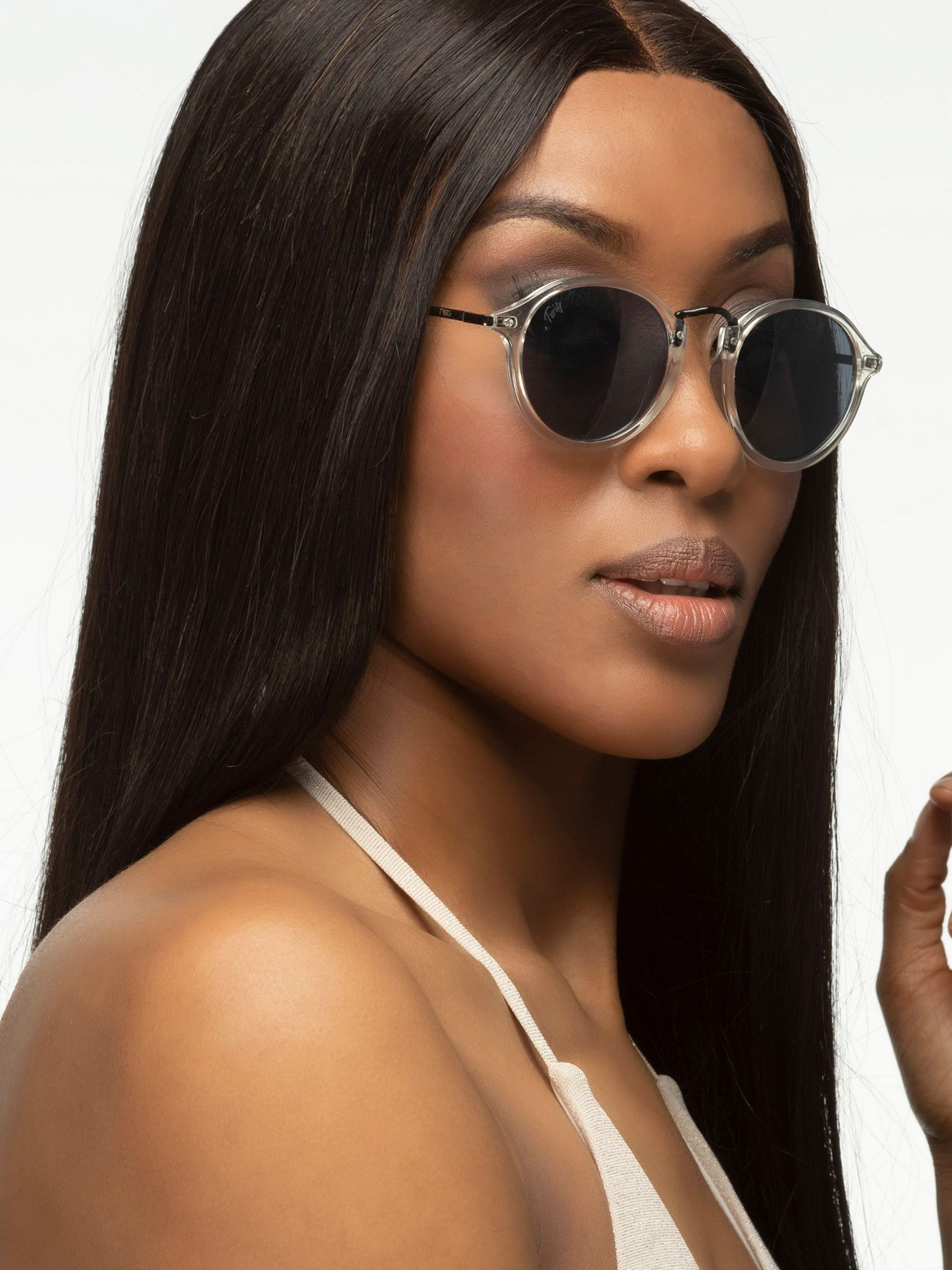Donna con occhiali da sole rotondi con montatura trasparente e lenti scure. Aste nere.