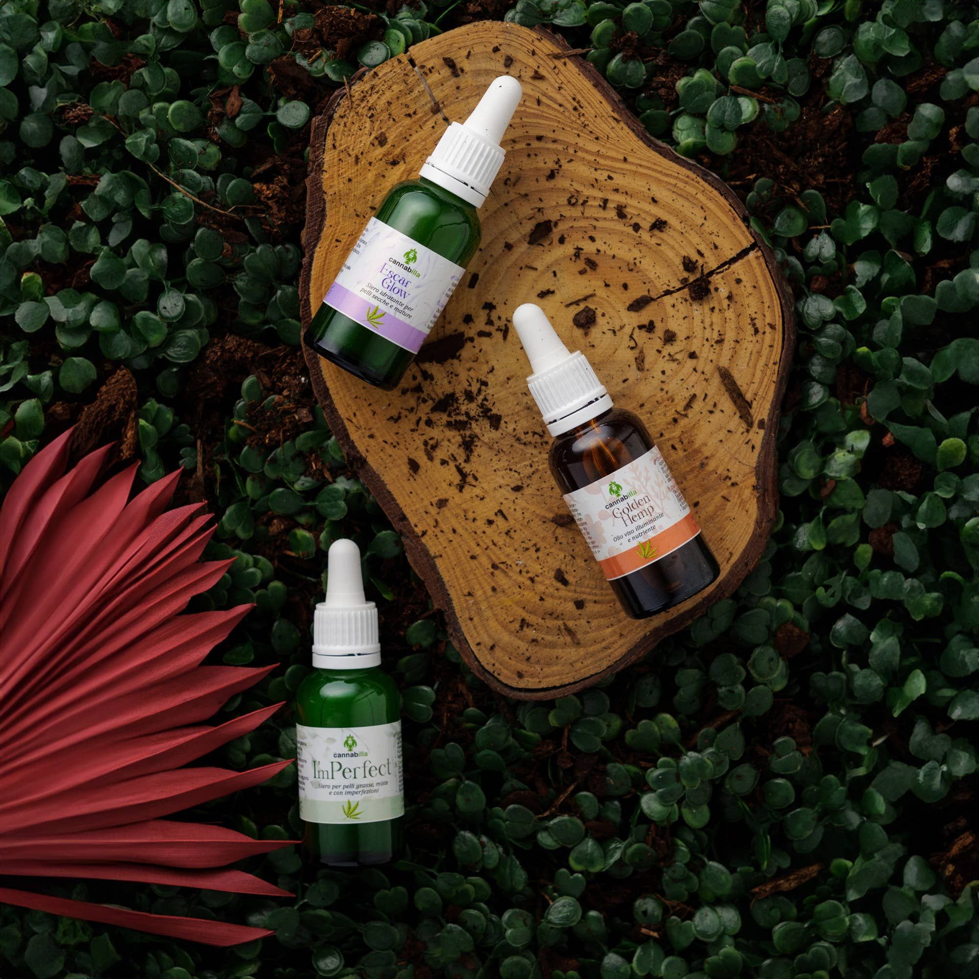 Tre flaconi su un ceppo. Scritta: Escar Glow, Perfect, Relaxed Hemp. Logo Cannabilla. Sfondo: foglie e una foglia rossa.