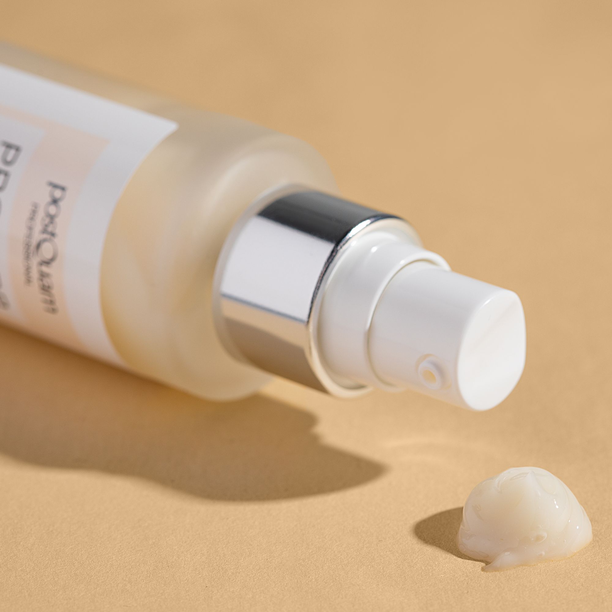 Flacone di siero con vaporizzatore. Goccia di siero su sfondo beige. Visibile: vaporizzatore, siero. Etichetta con scritta Postquam.