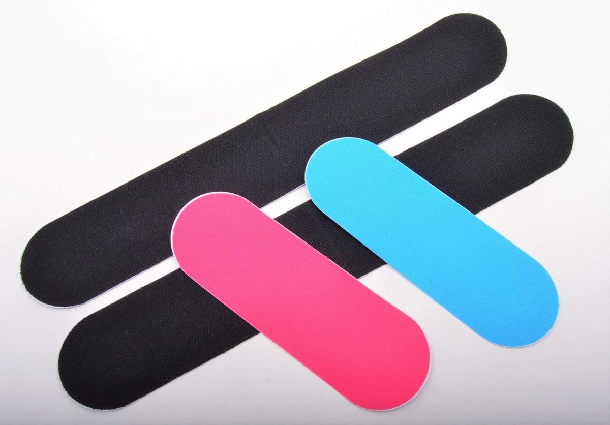 Tre cerotti kinesio rosa, blu e neri. I cerotti sono rettangolari e appoggiati su una superficie bianca.