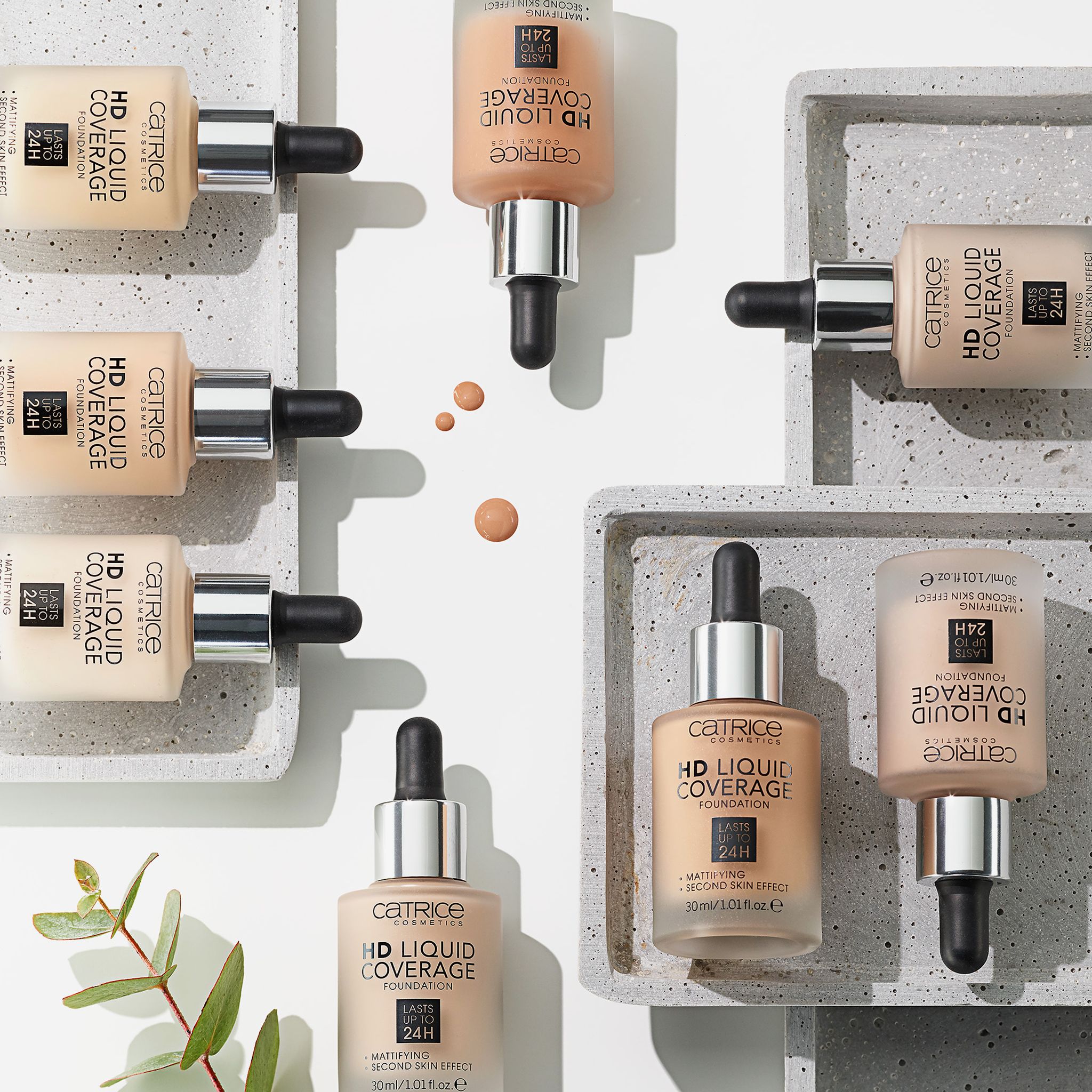 Diverse bottiglie di fondotinta liquido con pipette su vassoi. Scritta: HD Liquid Coverage Foundation. Opacizzante, resistente all'acqua, fino a 24 ore.