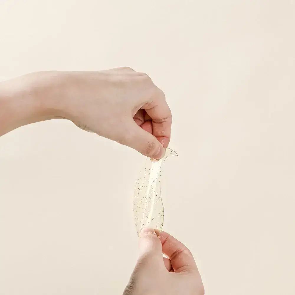 Mani che tengono un patch in gel per occhi. Patch trasparente con piccoli punti neri. Forma: curva.