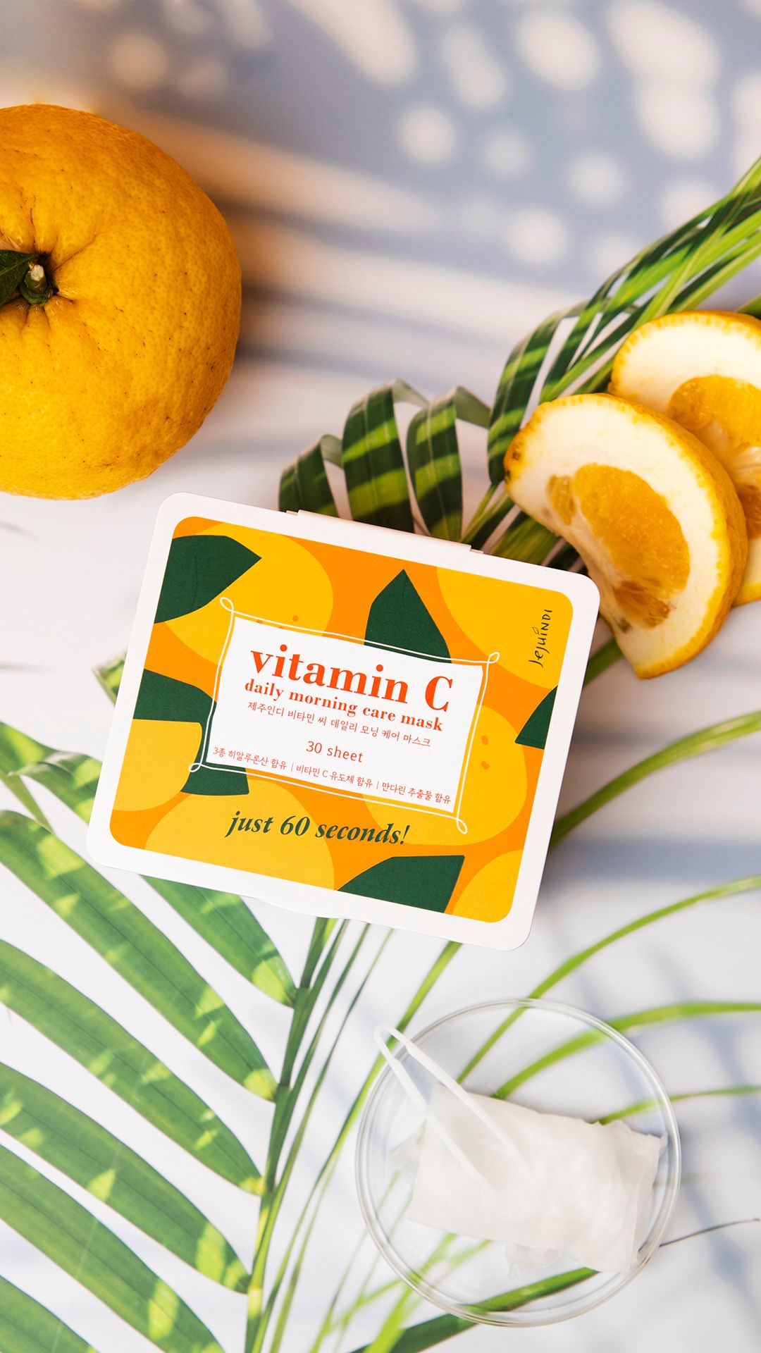 Scatola di maschere alla vitamina C. Scritta: Vitamin C Daily Morning Care Mask. Maschera e agrumi su fogliame.