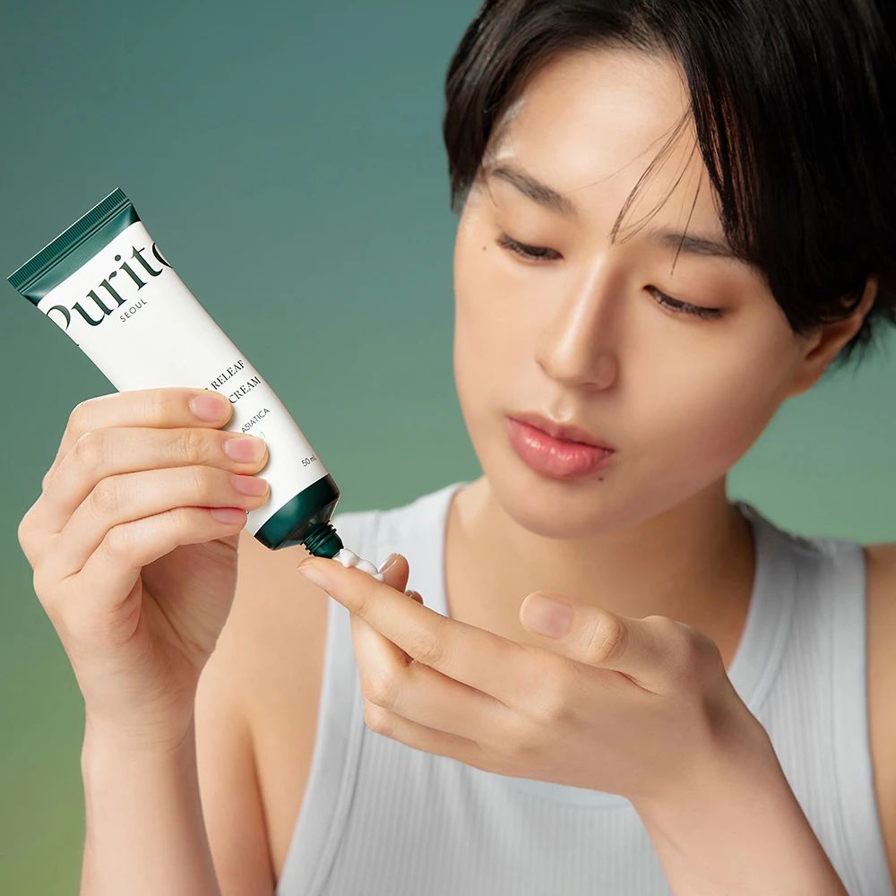 Donna che preme la crema da un tubetto sul dito. Tubetto con tappo verde e scritta: PURITO SEOUL, Wonder Releaf Centella Cream.