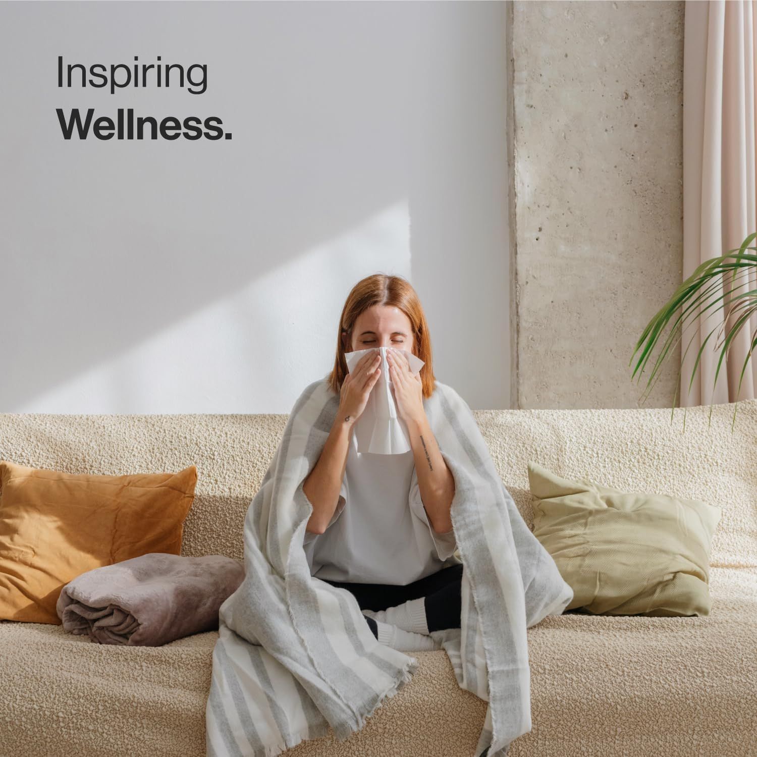 Persona sul divano con coperta e fazzoletto. Testo: Inspiring Wellness.