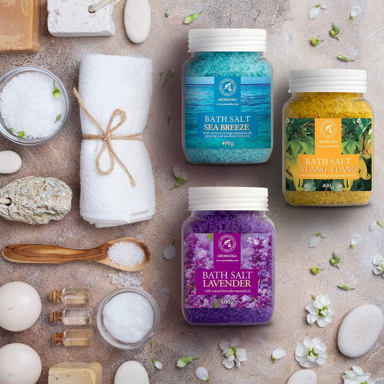 Tre barattoli di sali da bagno con accessori. Blu, giallo e viola. Scritte: Sea Breeze, Ylang-Ylang, Lavanda. Su un tavolo.