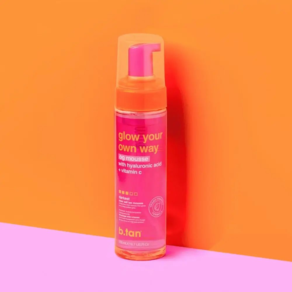 Flacone rosa con erogatore. Scritta: glow your own way og mousse con acido ialuronico + vitamina C. Marchio: b.tan.