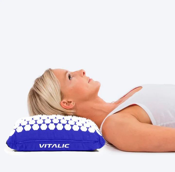 Donna sdraiata su cuscino di acupressione blu. Cuscino con punte bianche. Scritta: VITALIC.