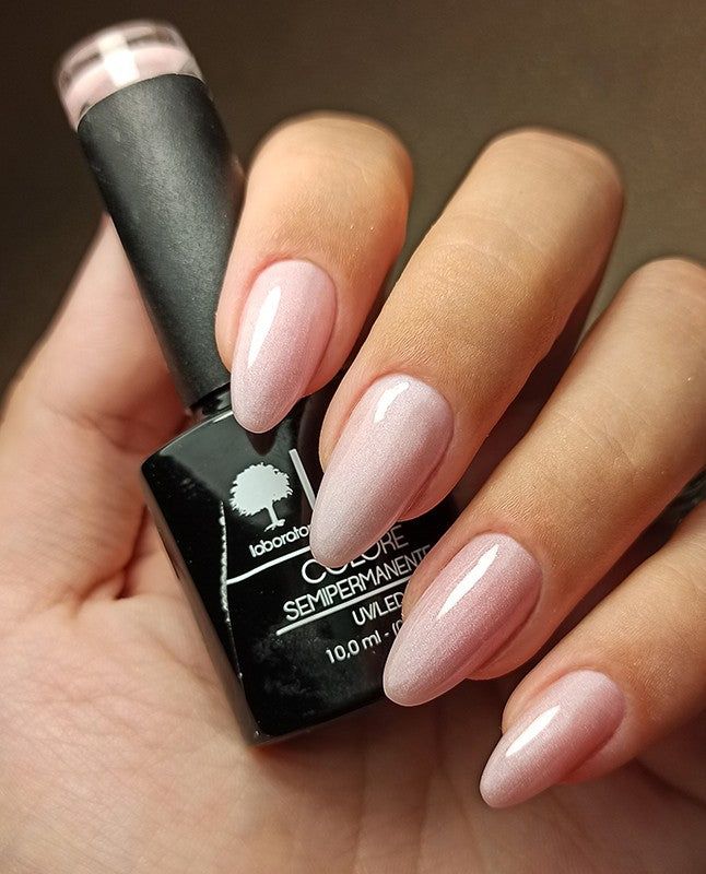 Mano con unghie smaltate e flacone di smalto. Rosa, lucido. Scritta: LCI, Colore Semipermanente.