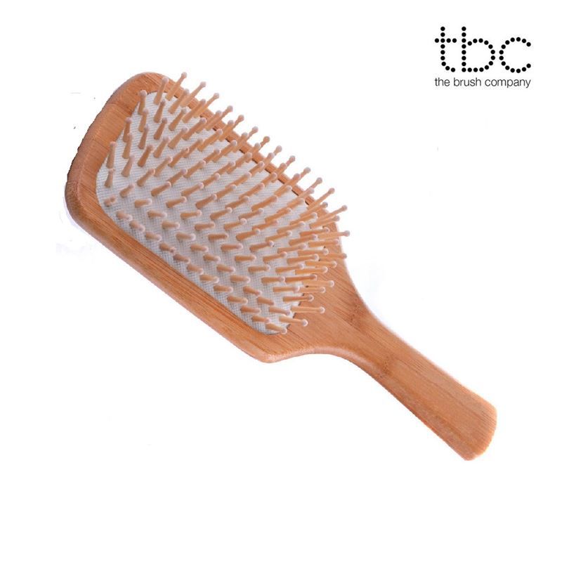 Spazzola per capelli in legno con logo 'tbc the brush company', testa rettangolare, denti in legno su cuscino bianco.