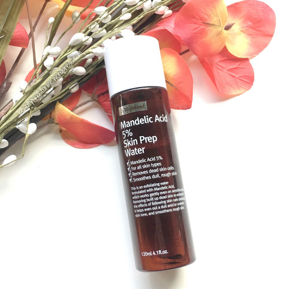 Flacone in vetro marrone con By Wishtrend Mandelic Acid 5% Skin Prep Water, circondato da fiori.