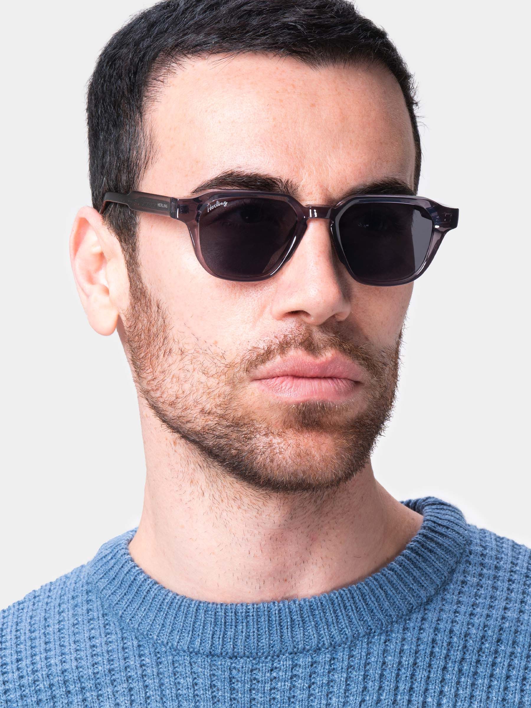 Primo piano di un uomo con occhiali da sole grigi. Il marchio Herling è visibile sull'asta.