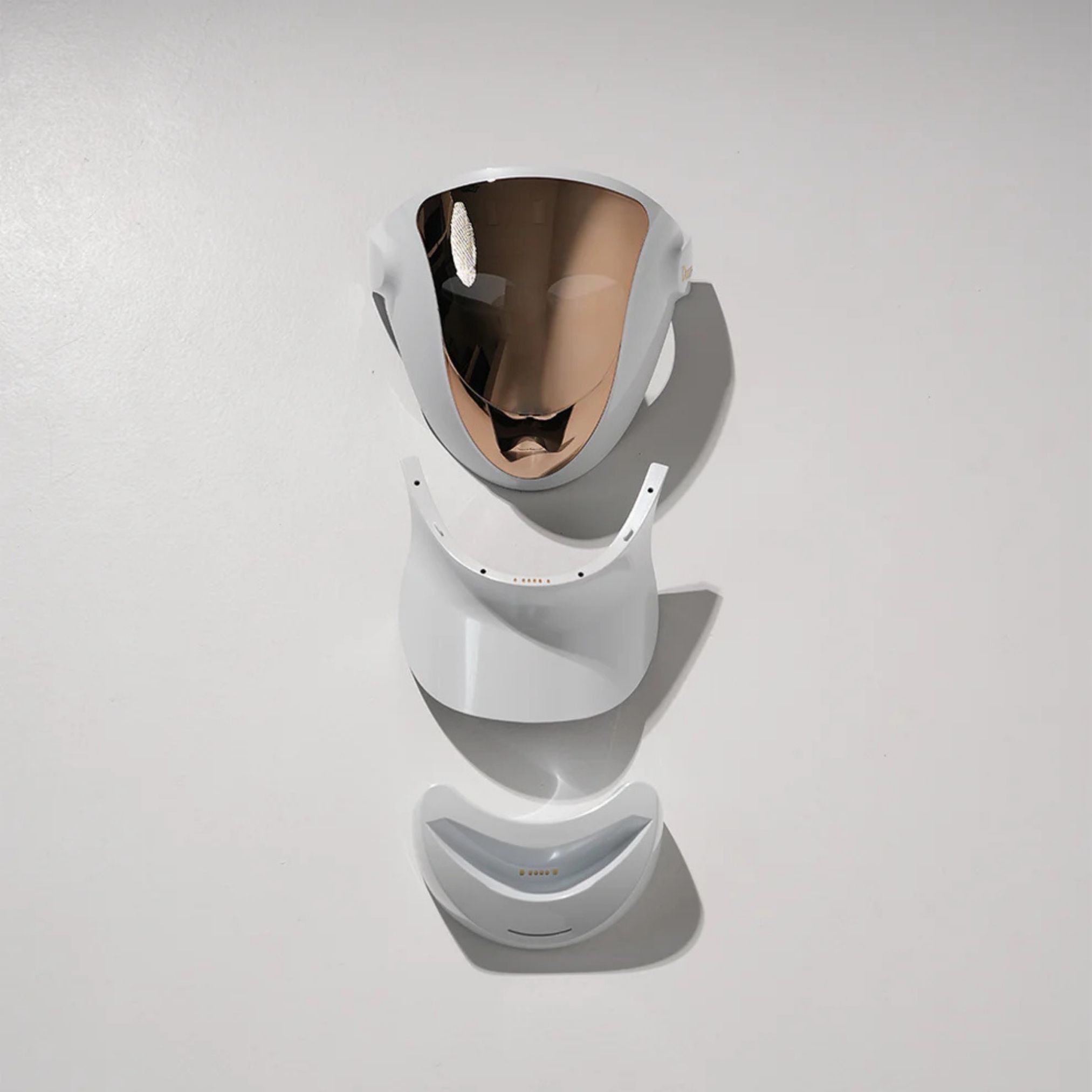 Maschera facciale smontata. Corpo bianco con superficie dorata. Composta da tre parti: maschera, estensione collo, mentoniera.