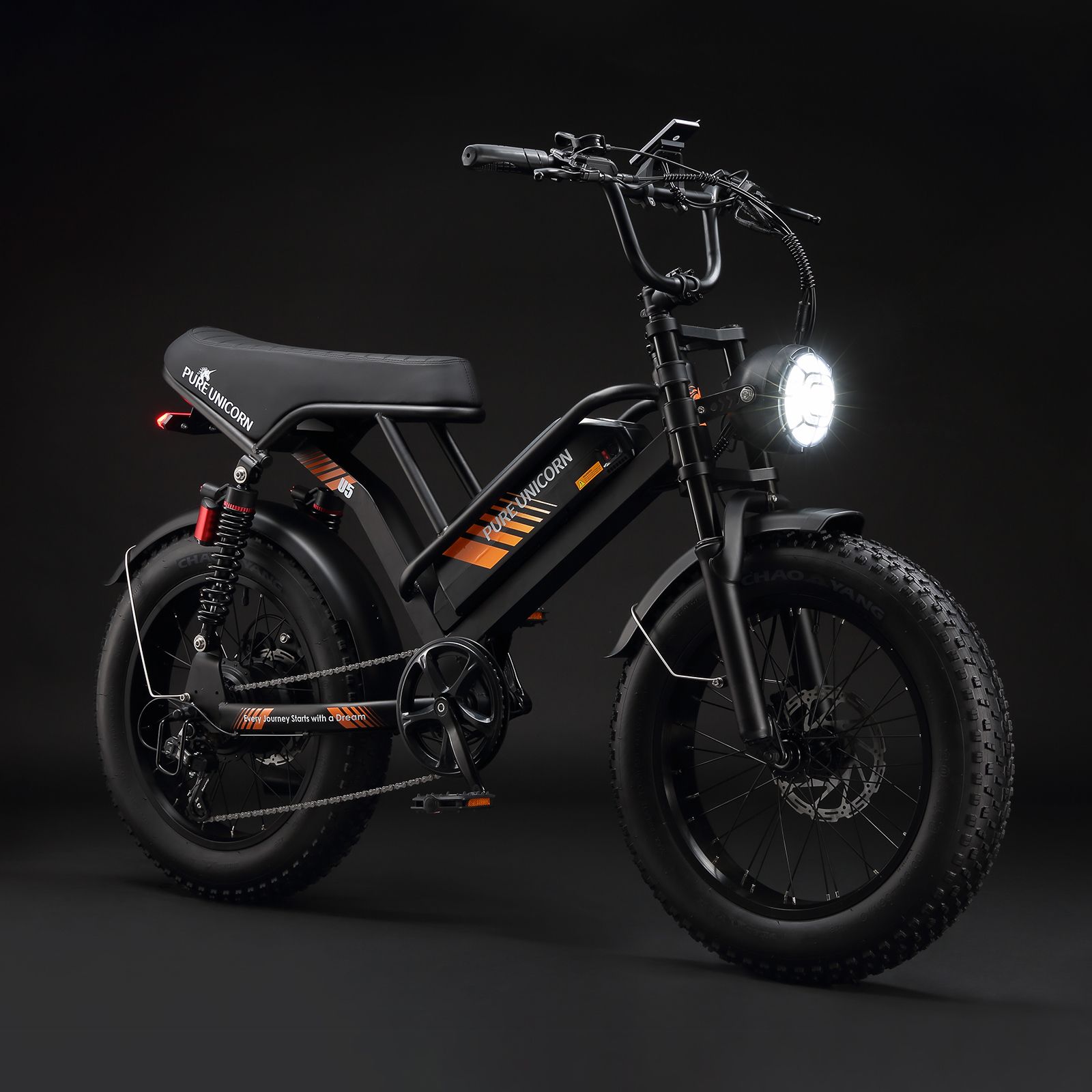 Bicicletta elettrica nera con pneumatici larghi, dettagli arancioni e scritta PURE UNICORN. Faro acceso.