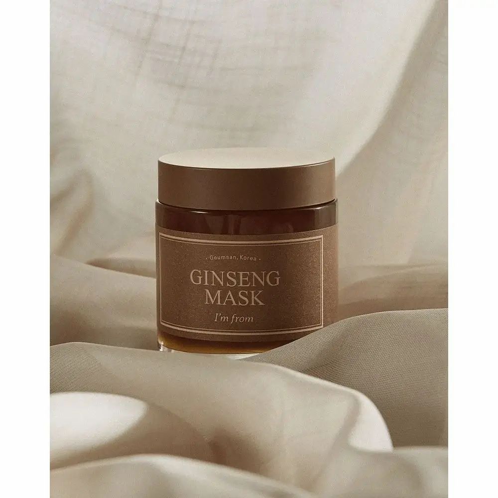 Barattolo di vetro con etichetta marrone. Scritta: GINSENG MASK, I'm from. Coperchio marrone. Su tessuto bianco.
