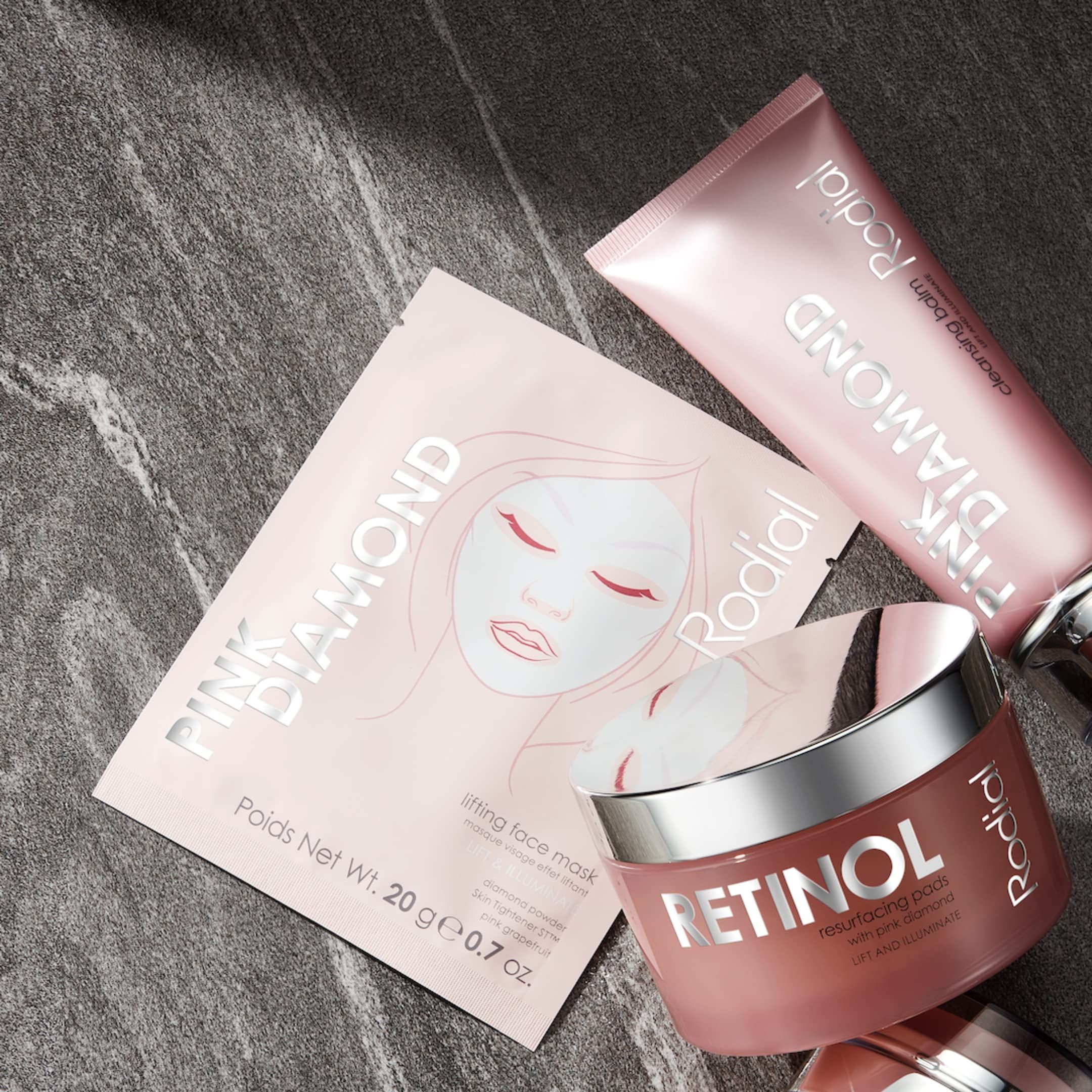 Maschera viso, balsamo detergente e crema al retinolo Rodial Pink Diamond rosa. Confezioni con nomi dei prodotti. Su sfondo grigio.