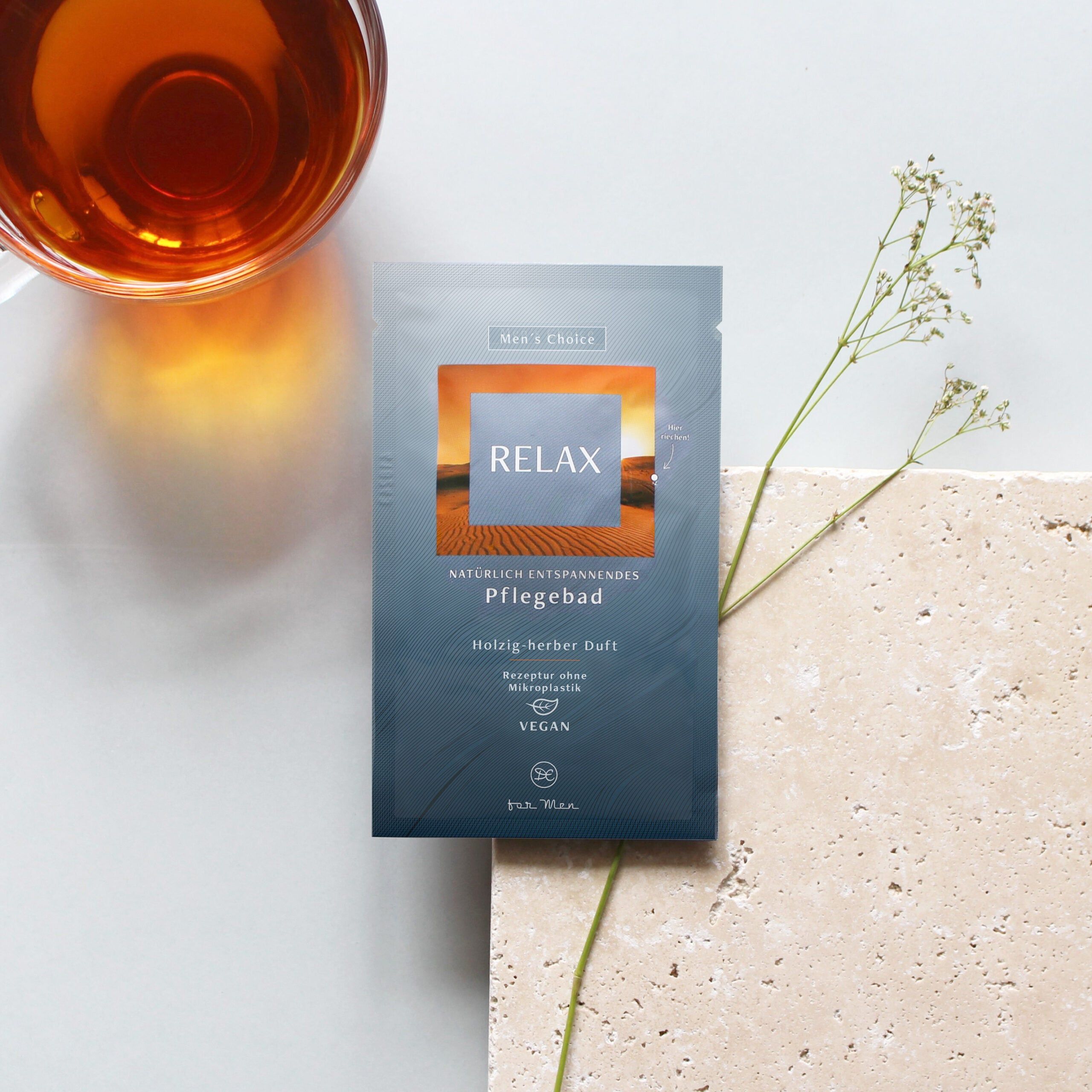 Confezione singola RELAX su superficie chiara. Accanto: bicchiere con liquido, pianta. Testo: Bagno curativo, profumo legnoso-erbaceo, vegano.