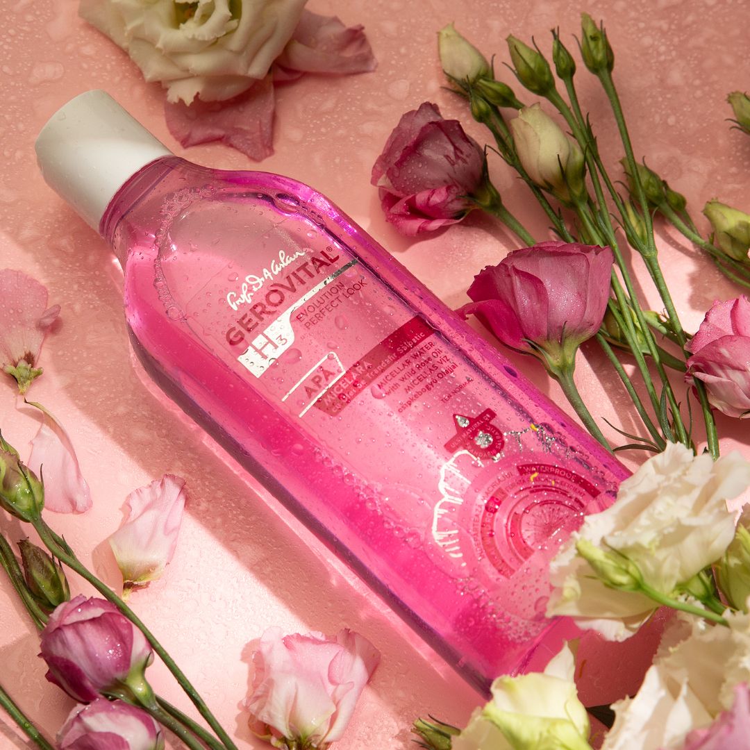 Liquido rosa in bottiglia trasparente con tappo bianco. Etichetta: Gerovital, Acqua Micellare. Circondato da fiori.