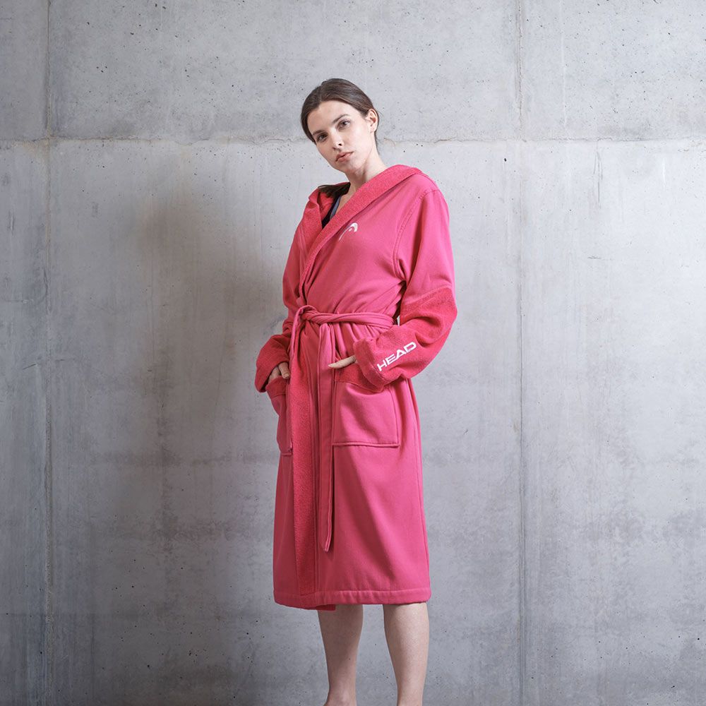 Una donna indossa un accappatoio rosa con cappuccio e cintura. La scritta "HEAD" è bianca sulla manica.