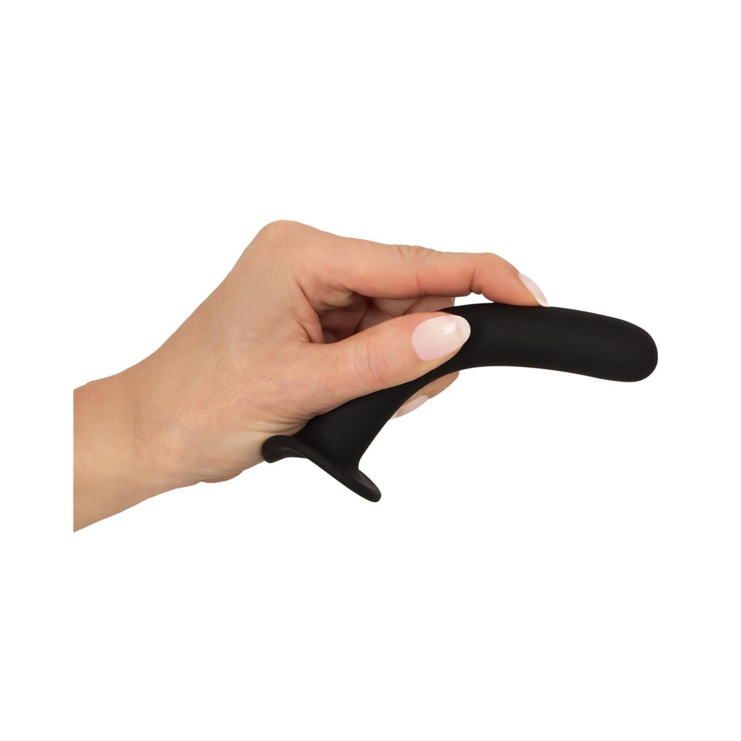 Dildo anale nero tenuto in una mano. Curvo, con base a ventosa. Silicone. Superficie morbida. Sfondo bianco.