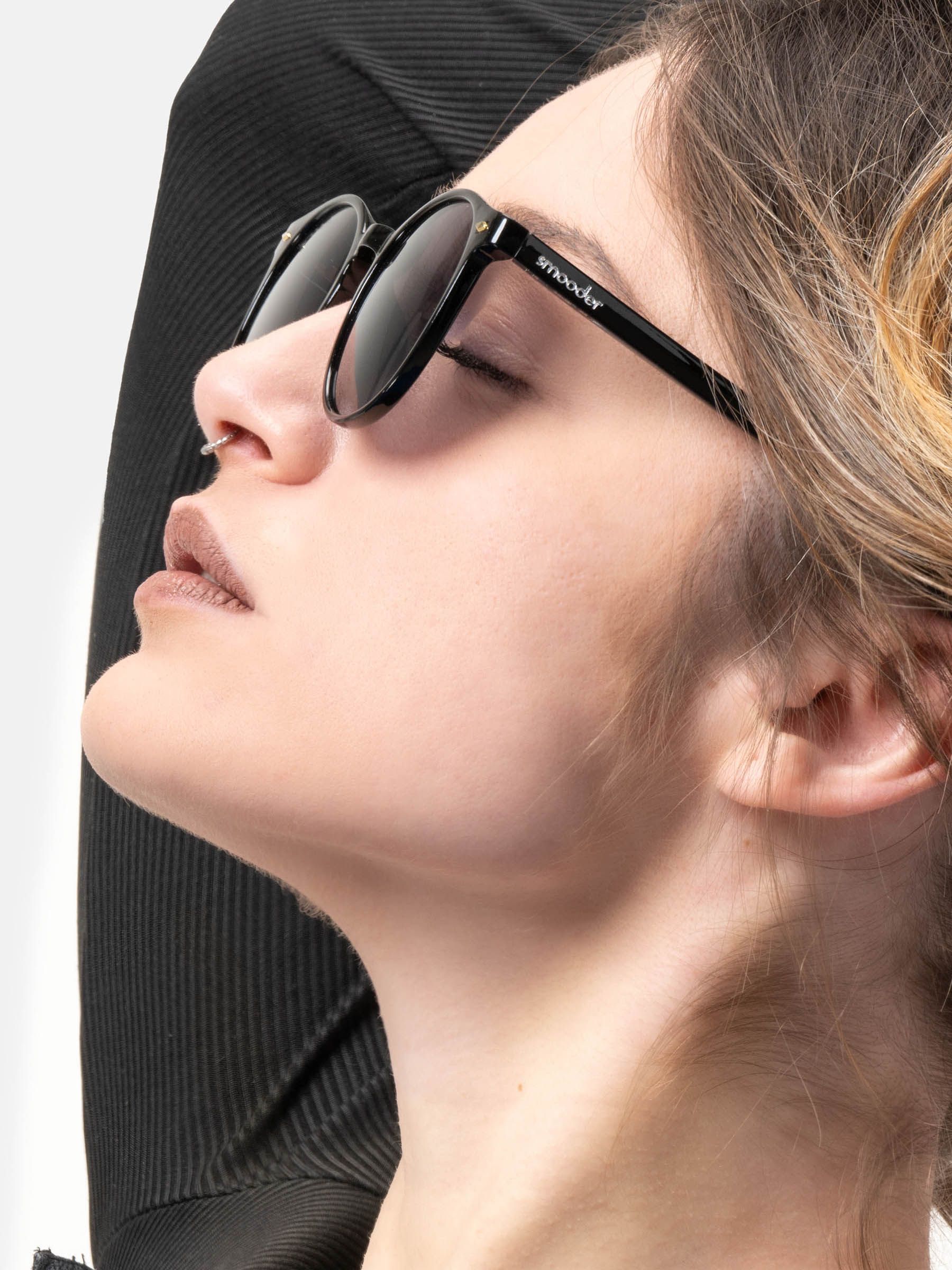 Persona che indossa occhiali da sole neri con lenti rotonde. 'smooder' è visibile sull'asta. Primo piano.