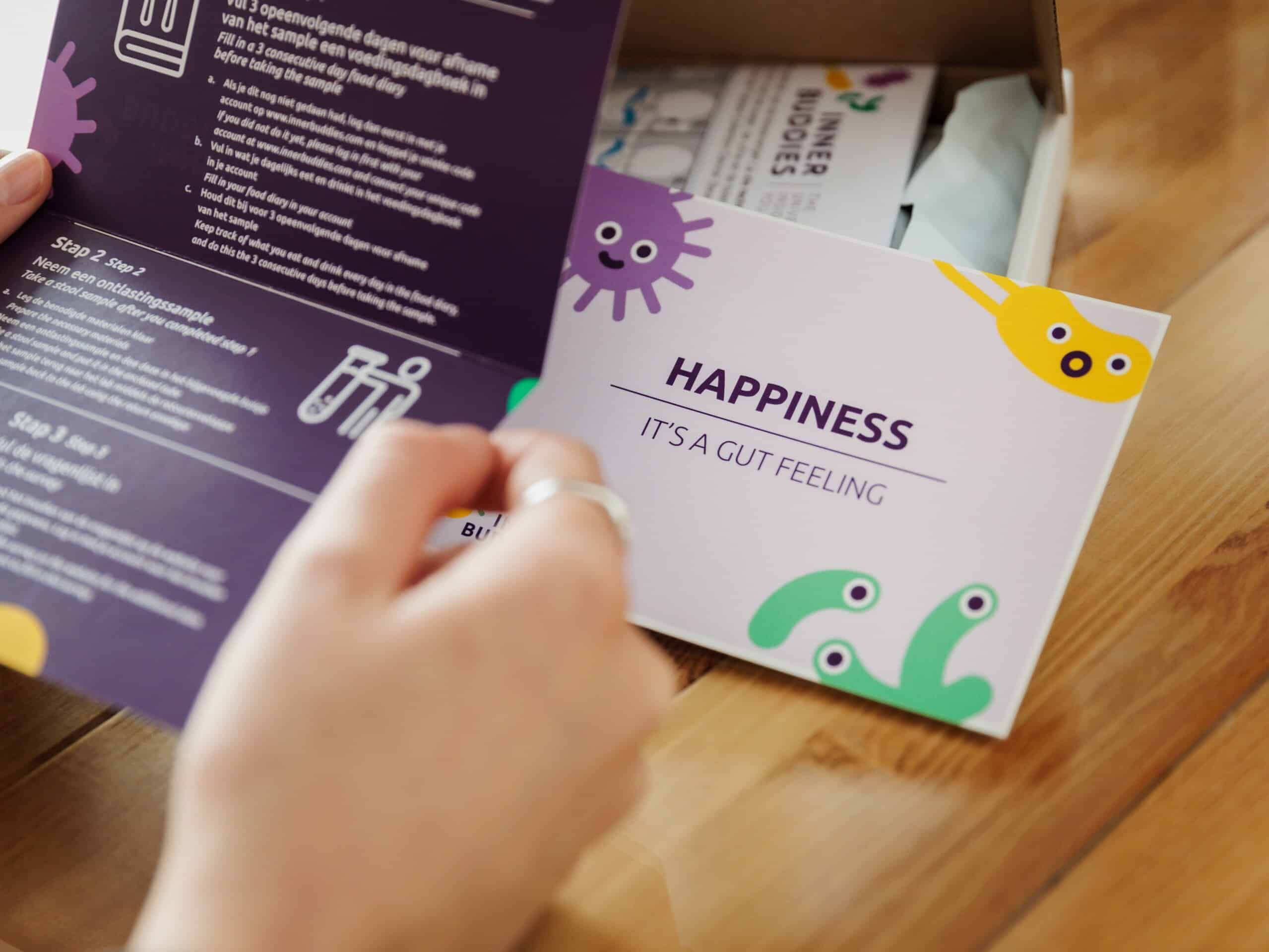 Persona che apre una brochure con istruzioni e un biglietto con scritto 'Happiness - It's a Gut Feeling'.