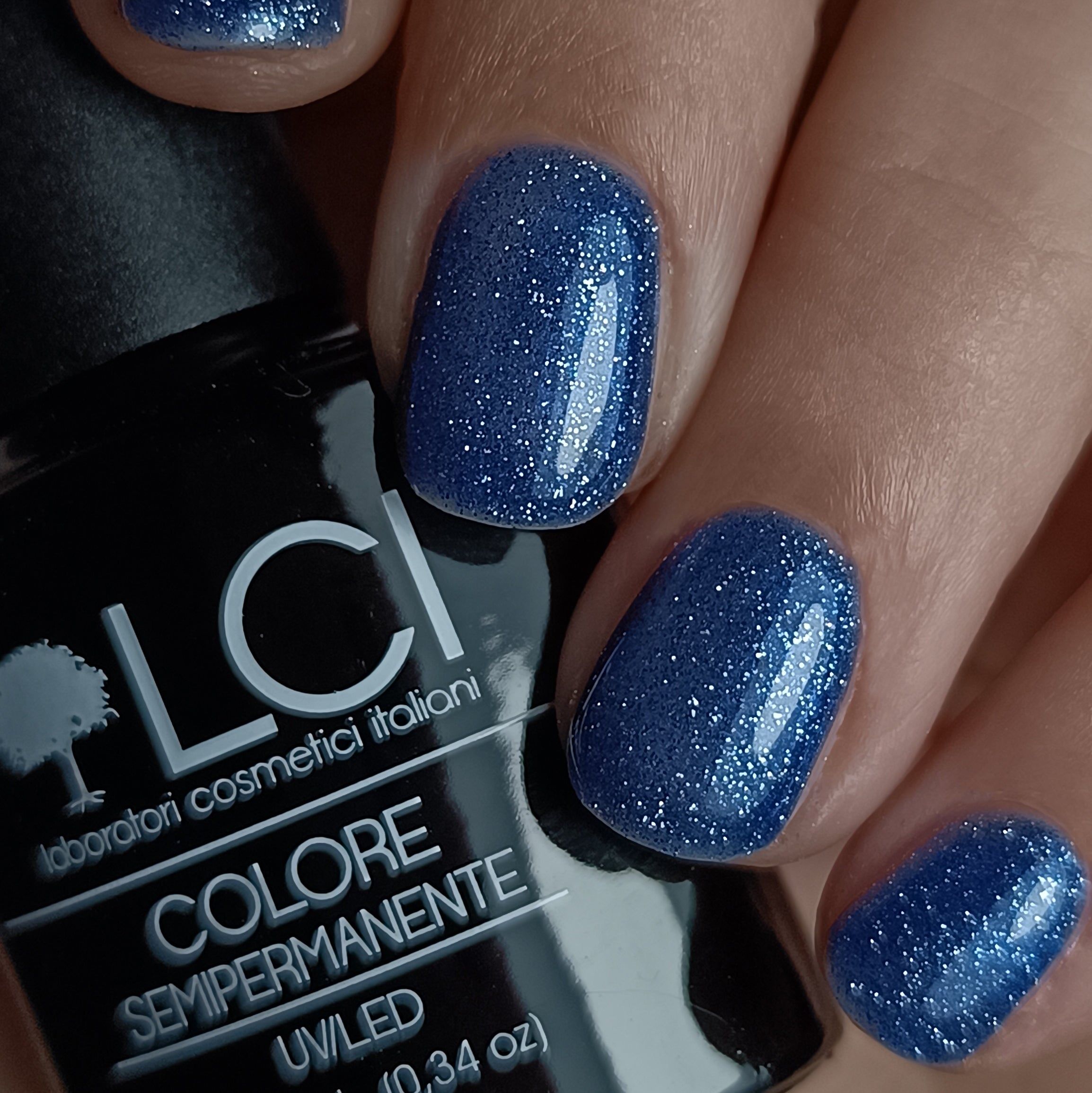 Smalto per unghie blu scuro glitterato sulle unghie. Flacone nero con testo sullo sfondo.