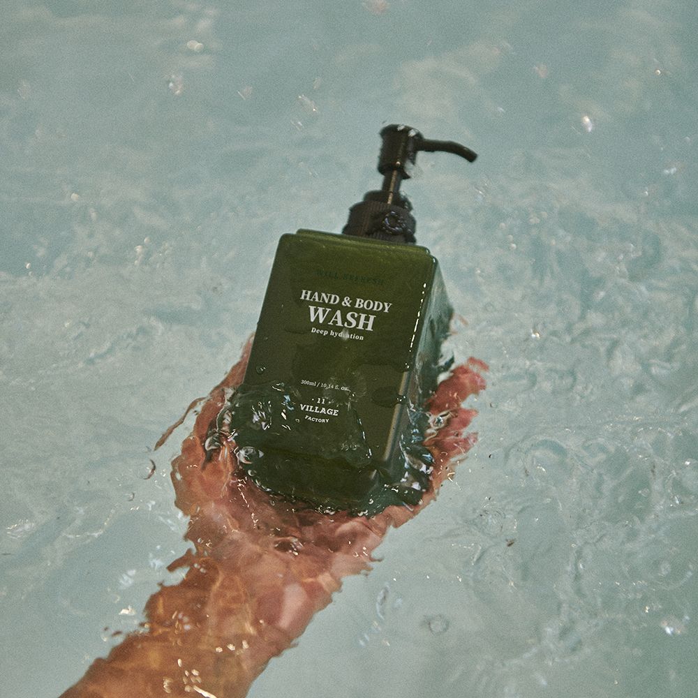 Flacone verde di lavaggio mani e corpo con dispenser nero in una mano, circondato dall'acqua. Scritta: Hand & Body Wash.