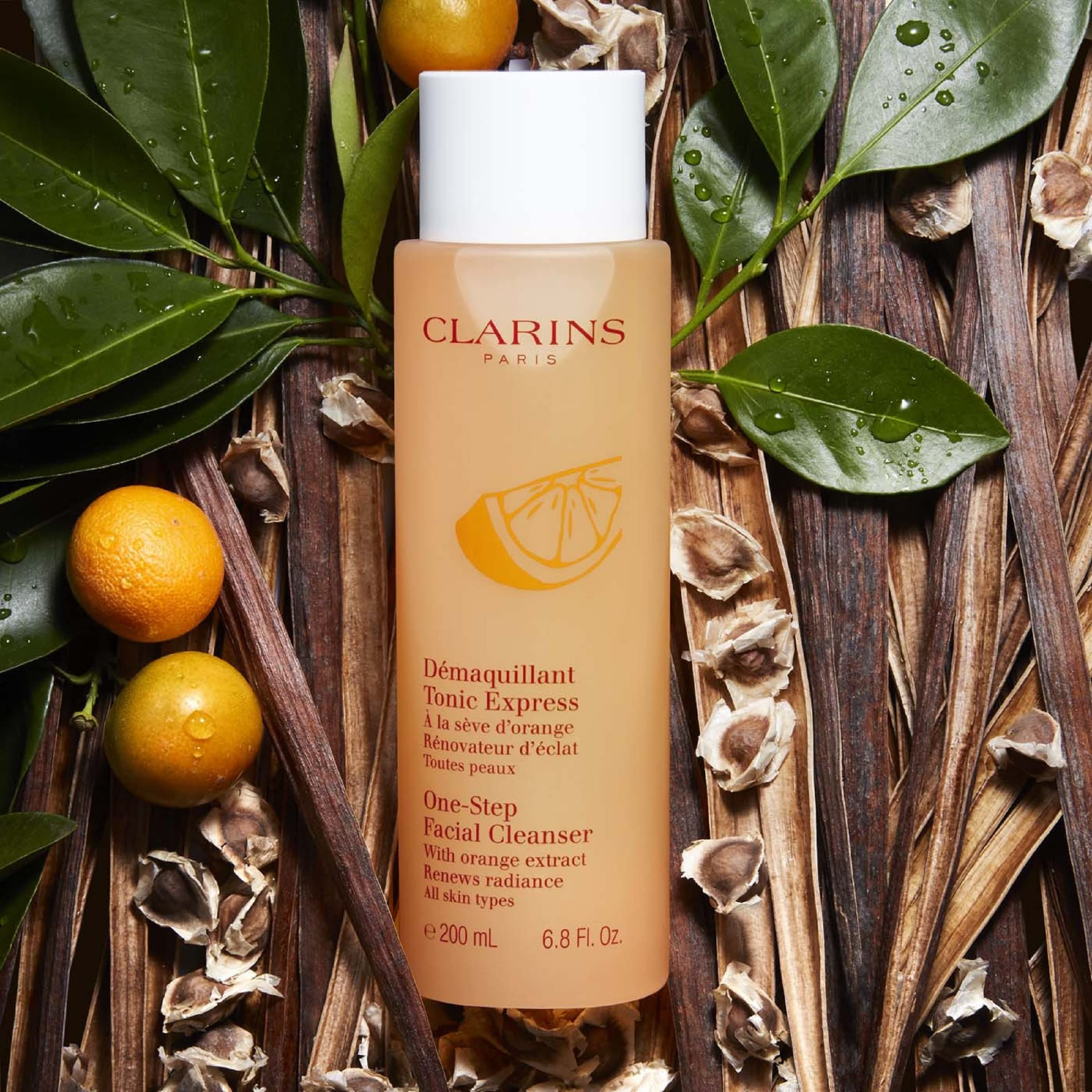 Flacone arancione con tappo bianco, circondato da foglie e arance. Scritte: Clarins Paris, D
emaquillant Tonic Express.