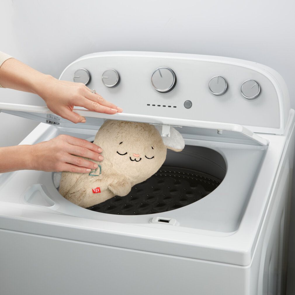 Coniglietto di peluche in lavatrice. Sportello aperto, mani che tengono il giocattolo.