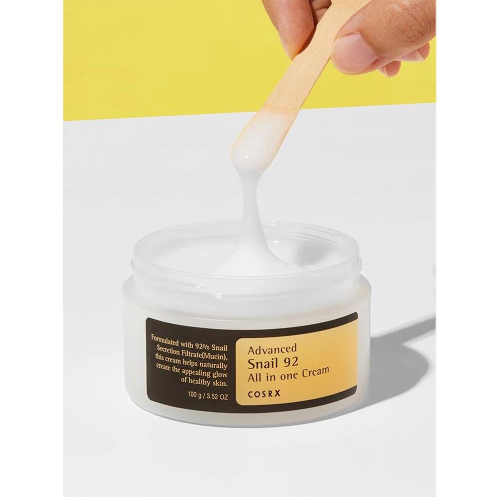 Vasetto di crema COSRX All in One con spatola che preleva una crema bianca.