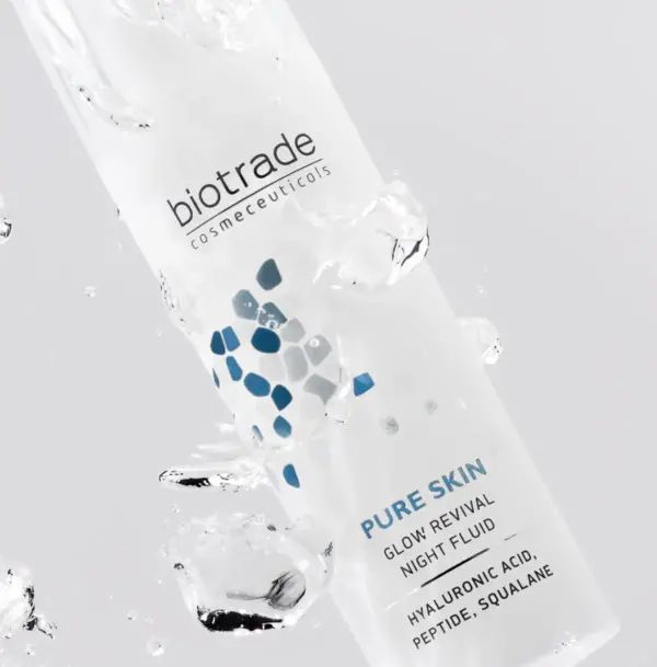 Flacone bianco con pompa e tappo trasparente. Scritta: Biotrade, Pure Skin Glow Revival Night Fluid. L'acqua circonda il prodotto.