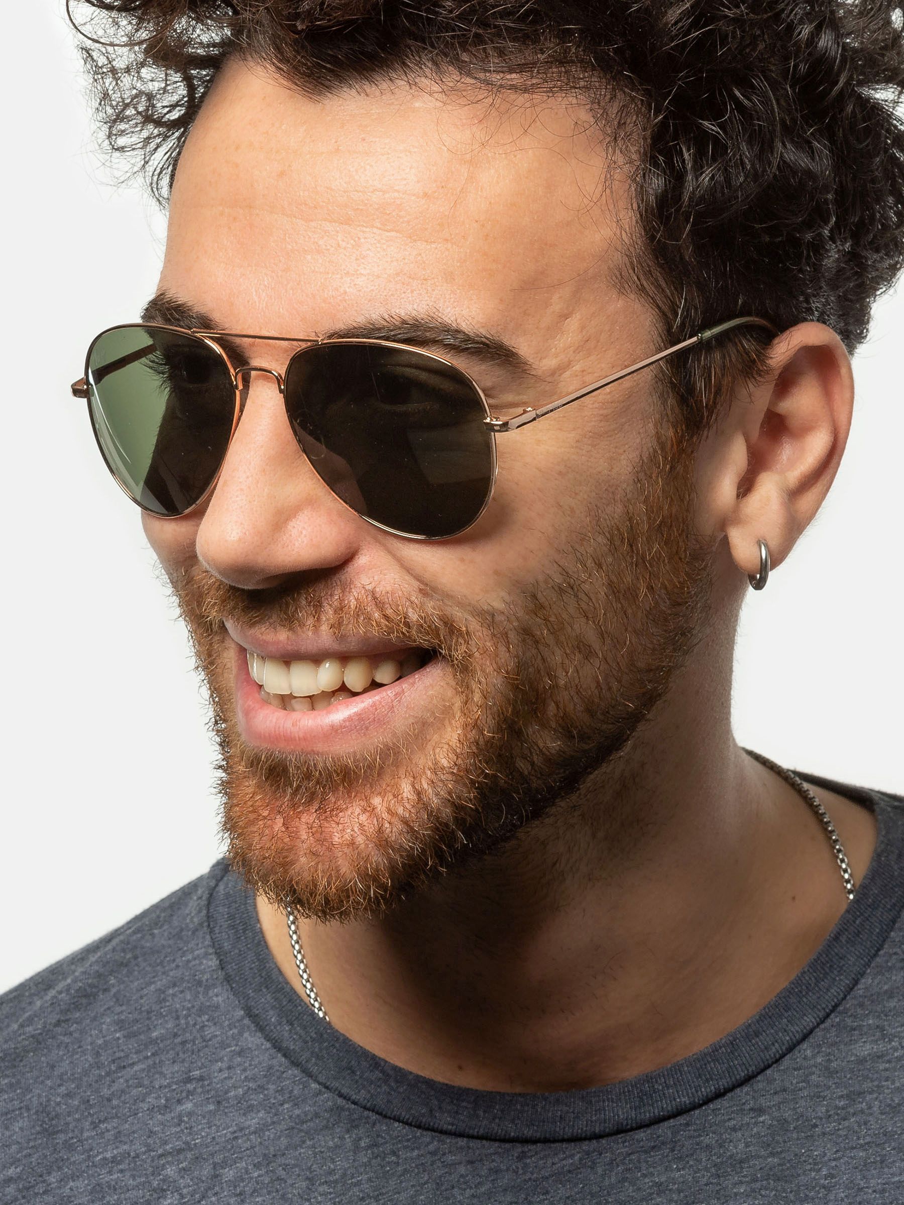 Uomo con occhiali da sole dorati e lenti verdi. Visibili barba e collana.