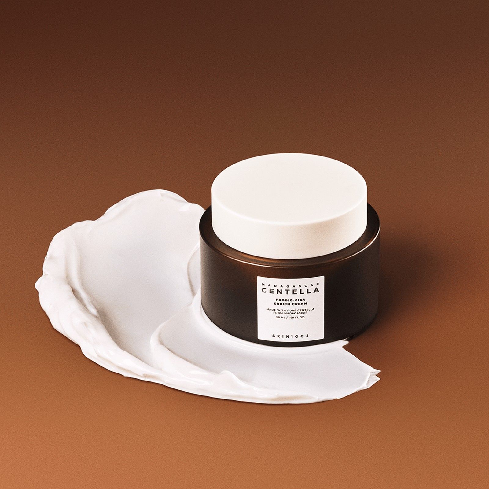 SKIN1004 Madagascar Centella Probio-Cica Enrich Cream con una striscia di crema su sfondo marrone.