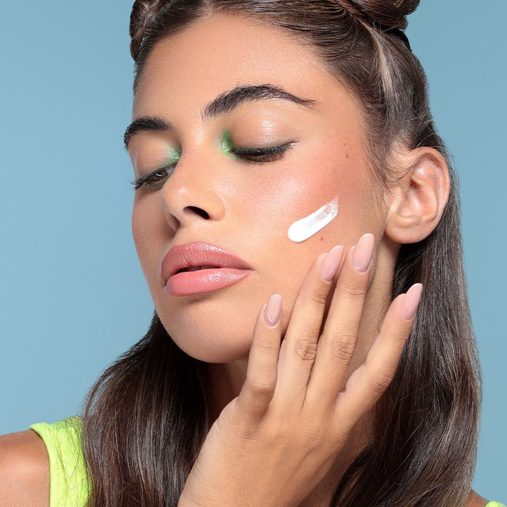 Donna applica crema sul viso. Sulla pelle si vede una macchia di crema.