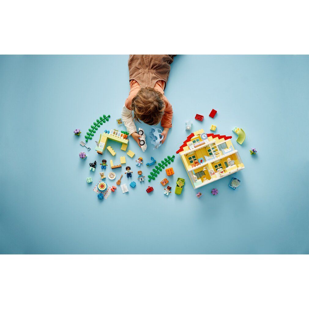 Bambino gioca con LEGO Duplo Casa famiglia 3-in-1. Casa gialla, personaggi, auto, scivolo e accessori su sfondo blu.